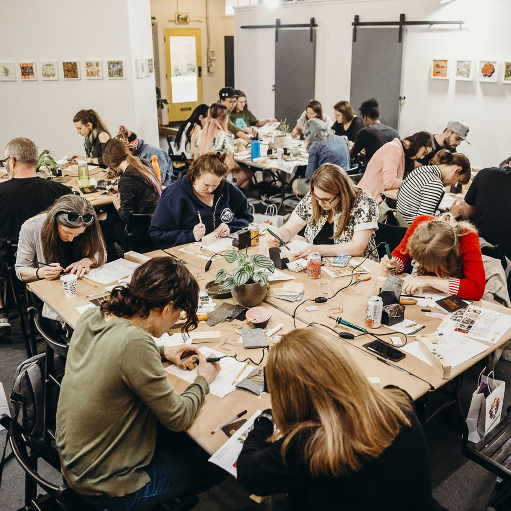 Dozens of people gathered around large tables making art in a cannabis safe space